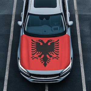 May include: A silver car with a red hood cover featuring the Albanian flag. The flag has a black double-headed eagle on a red background.