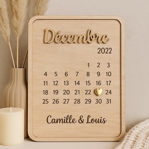 Peut inclure: Calendrier en bois pour décembre 2022, avec le nom du mois et l'année dans une police décorative. Le calendrier comprend les jours du mois, avec un cœur marquant le 22. Les noms "Camille & Louis" sont en bas.