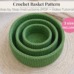 May include: Three green crochet baskets of varying sizes nested together, with the text "Crochet Basket Pattern" and "Step by Step Instructions (PDF + Video Tutorial)". A pink circle indicates "3 sizes included". The baskets are on a beige woven mat.