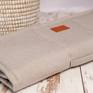 Peut inclure: Un coussin en lin beige avec un patch en cuir marron. Le coussin est pli&eacute; en trois et a un bouton sur le c&ocirc;t&eacute;.