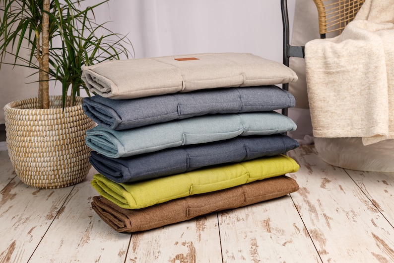 Peut inclure: Une pile de six housses de coussin de couleurs diff&eacute;rentes. Les coussins sont faits d'un tissu doux et textur&eacute; et ont un design matelass&eacute;. Les couleurs sont beige, bleu, bleu clair, bleu fonc&eacute;, vert et marron.