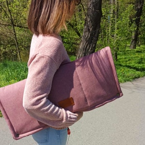 Peut inclure: Un coussin matelass&eacute; rose avec un patch en cuir marron. Le coussin est tenu par une personne portant un pull rose.