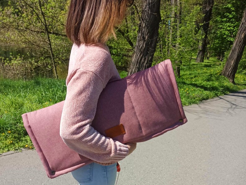 Peut inclure: Un coussin matelass&eacute; rose avec un patch en cuir marron. Le coussin est tenu par une personne portant un pull rose.