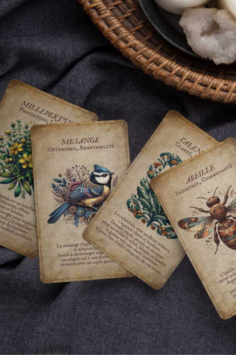 May include: A collection of vintage-style oracle cards with botanical and animal illustrations. The cards feature images of a blue bird, a bee, and various plants, with French text. The cards are arranged on a dark gray fabric.