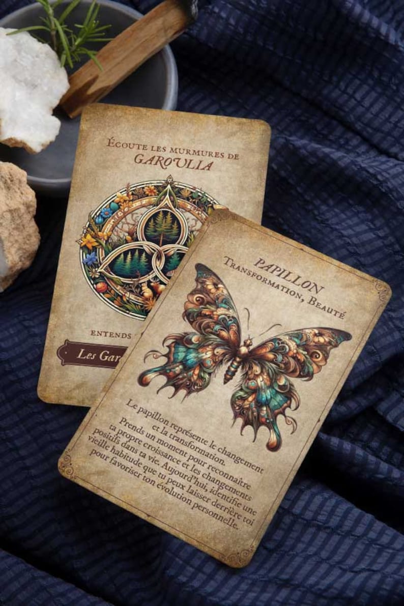 May include: Two tarot cards with vintage-style illustrations. One card features a detailed butterfly design with teal, brown, and orange hues. The other card has a circular design with a forest scene. Text includes "PAPILLON" and "GAROULIA".