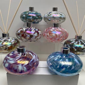 May include: A collection of decorative glass diffuser bottles in shades of blue, pink, and purple. Each bottle features a silver collar and contains a decorative liquid and reeds for fragrance diffusion. The bottles are arranged on clear acrylic shelves.