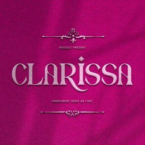 May include: A pink fabric background with a white embroidered font that says "PROUDLY PRESENT" above the word "CLARISSA" in a decorative font. Below the word "CLARISSA" is the text "EMBROIDERY SERIF BX FONT".