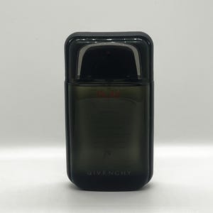 May include: A rectangular, dark-tinted perfume bottle with a black cap. The bottle has a curved top and the word "GIVENCHY" is printed in white at the bottom. The perfume bottle is set against a white background.