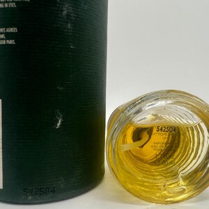 May include: A perfume bottle with a clear, textured glass base and a dark green cylindrical container. The bottle contains a yellow liquid. The text "542504" is visible on the bottle and container. The bottle is labeled "VAPORISATEUR EAU DE PARFUM" and contains 60 ml.