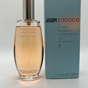 Könnte beinhalten: Eine Parfümflasche und -schachtel. Die Flasche ist klar mit einem silbernen Verschluss und enthält eine hellorangefarbene Flüssigkeit. Die Schachtel ist hellblau mit den Worten "JOOP! Rococo" in Rot und Weiß. Die Flasche ist mit "silken deodorant natural spray eau déodorante" beschriftet. Auf der Schachtel steht "3.4 FL OZ e 100 ml".