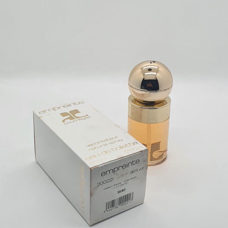 May include: A perfume bottle and box set. The bottle has a gold cap and a clear glass body with a light amber liquid. The box is white with the word "empreinte" and the brand name. The box also has the text "eau de toilette".