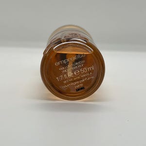 May include: A bottle of Empreinte eau de toilette. The bottle is amber-colored with a gold cap. The label reads "empreinte eau de toilette vaporisateur 1.7 fl.oz e 50 ml". The brand is Courr&egrave;ges Parfums, Paris.