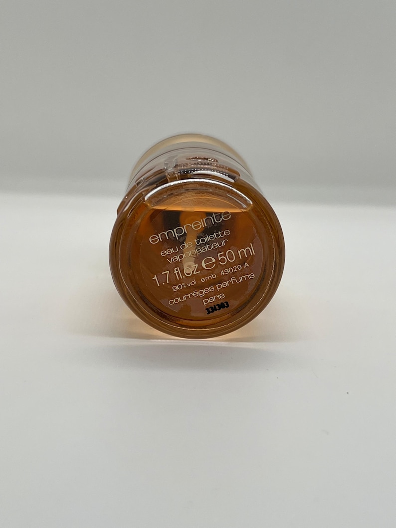 May include: A bottle of Empreinte eau de toilette. The bottle is amber-colored with a gold cap. The label reads "empreinte eau de toilette vaporisateur 1.7 fl.oz e 50 ml". The brand is Courr&egrave;ges Parfums, Paris.