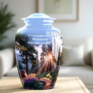 May include: A glossy, cylindrical cremation urn featuring a vibrant forest scene with tall pine trees, a sunlit path, and purple wildflowers. The text "In Loving Memory of Florence Dec/1956 - Jan/2025" is printed in white on the front of the vessel.