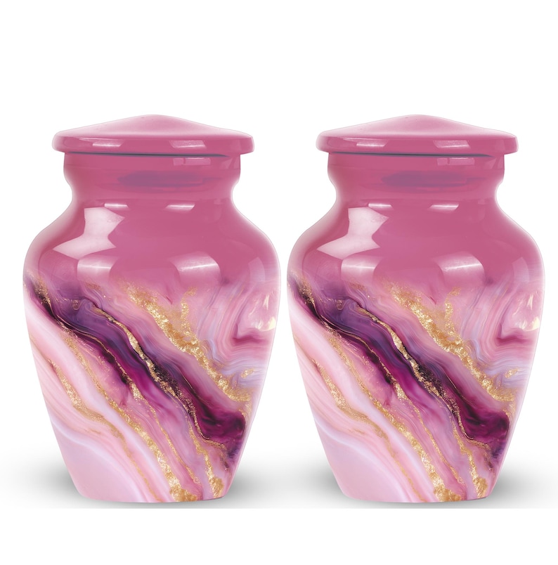May include: Two pink urns with a swirling design of purple, white, and gold. The urns have a glossy finish and a matching lid. The design resembles marble or agate, creating an elegant and unique appearance.