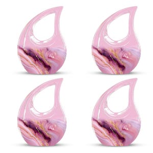 May include: Four teardrop-shaped decorative objects with a handle. The objects have a pink, translucent handle and a marbled design in shades of pink, purple, and gold. The objects are arranged in a square formation.
