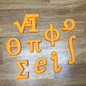 Può includere: Lettere di plastica arancione che rappresentano simboli matematici, tra cui le lettere greche theta, pi, phi, sigma e omega, nonché i simboli di radice quadrata, integrale e il numero e.