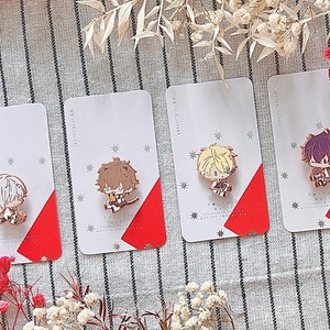 Puede incluir: Cuatro tarjetas blancas con acentos rojos que presentan diferentes pines de esmalte de personajes de anime. Los pines son de color dorado y presentan personajes con cabello castaño, rubio y morado.
