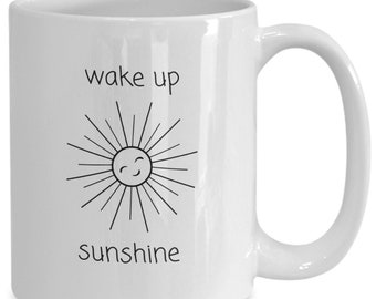 May include: White ceramic coffee mug with black text that reads "wake up sunshine" and a simple line drawing of a smiling sun.
