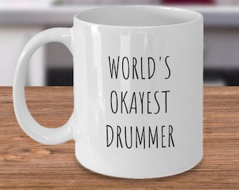 May include: White ceramic coffee mug with black text that reads "World's Okayest Drummer".