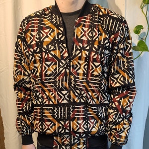 Könnte beinhalten: Eine schwarze Bomberjacke mit einem geometrischen Muster in Braun-, Weiß- und Orangetönen.