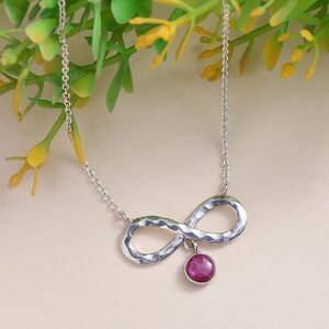May include: A silver infinity necklace with a hammered finish and a dangling pink gemstone pendant.