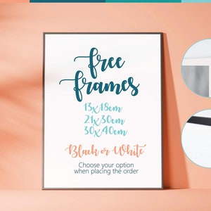 May include: A white poster with the text "free frames" in blue cursive lettering. The poster lists three frame sizes in centimeters: 13x18cm, 21x30cm, and 30x40cm. The poster also states "Black or White" and "Choose your option when placing the order". The poster is framed in a black frame and is displayed on a peach-colored surface.