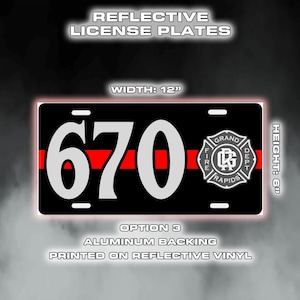 May include: Black license plate with white "670" and a red stripe. Features the Grand Rapids Fire Dept. logo. Plate dimensions are 30.5 cm wide and 15.2 cm high.