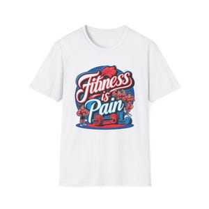 Può includere: T-shirt bianca con un design grafico. Il design presenta il testo "Fitness is Pain" in un font stilizzato, insieme a illustrazioni di bodybuilder e attrezzature da palestra. Il design utilizza colori rosso, blu e bianco.