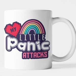 Può includere: Tazza in ceramica bianca con manico. La tazza presenta un design con un cuore rosso pixelato con la scritta "MY" e un arcobaleno sopra le parole "LITTLE Panic ATTACKS" in un carattere giocoso. La tazza è di dimensioni standard.