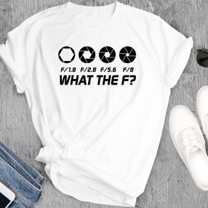 Könnte beinhalten: Weißes T-Shirt mit einer schwarzen Grafik von Kamera-Blendenwerten: F/1.8, F/2.8, F/5.6 und F/8, und dem Text "WHAT THE F?". Das Shirt wird mit Jeans, weißen Schuhen und Sonnenbrille präsentiert.