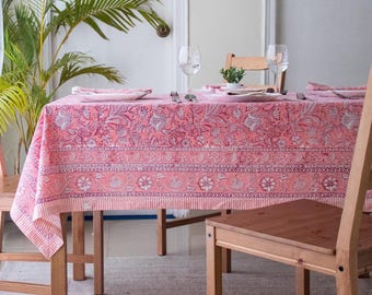 May include: A rectangular tablecloth featuring a coral pink base with a dark pink floral and vine block print pattern. The design includes horizontal borders with geometric and botanical motifs, finished with a striped edge along the bottom hem.