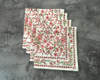 May include: A set of four square cloth napkins featuring an off-white base with a repeating floral pattern in shades of red and pink, accented by green vines and leaves. Each napkin has a distinct border design with a thin red and green line.