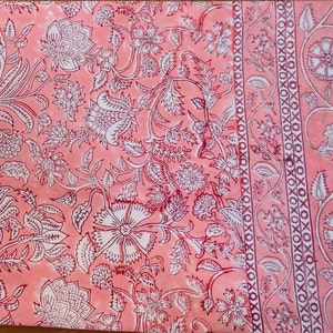 May include: A pink fabric with a white floral pattern. The fabric has a border with a repeating pattern of white circles and Xs.