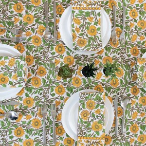 Mustard Floral Block-print cotton Tablecloth lay out on a table with a set of 4 napkins placed on white porcelain plates and cutlery beside each plate.