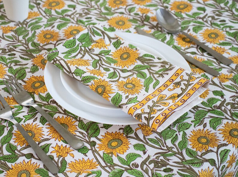 cotton floral Mustard block print tablecloth in Sunflowers design with single napkin displayed on a white porcelain plate. This makes a perfect mothers day gift.