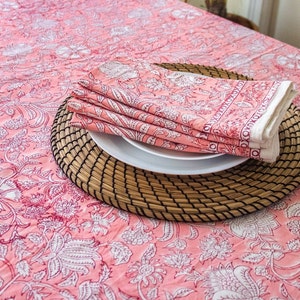 May include: Pink floral tablecloth with a woven placemat and folded pink floral napkins on top of a white plate.