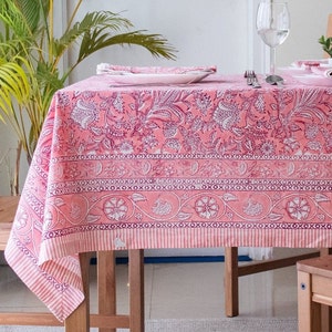 May include: A pink floral tablecloth with a white border and a repeating pattern of 'x's. The tablecloth is laid on a wooden table with two chairs.