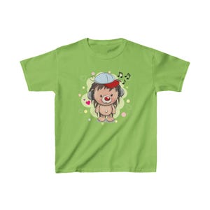 Könnte beinhalten: Ein grünes T-Shirt mit einem Comic-Igel, der eine blaue und rote Baseballkappe und Kopfhörer trägt. Der Igel ist von rosa Herzen und Noten umgeben.