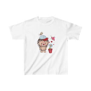 May include: White t-shirt with a cartoon hedgehog wearing a blue hat and holding a flower in a red pot. There are two pink butterflies and hearts in the design.