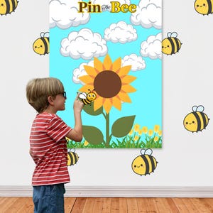 May include: A "Pin the Bee" party game with a sunflower and bee theme. The game board features a blue sky with clouds and a large sunflower. The words "Happy Bee Day" and "Print, Cut, Play" are visible.