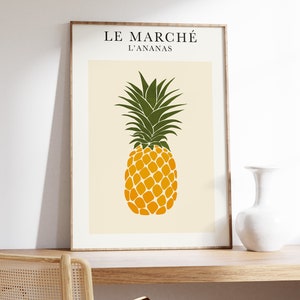 Op de afbeelding: Een ingelijst print met een gele ananasillustratie en de tekst "LE MARCHÉ L'ANANAS" op een crèmekleurige achtergrond.