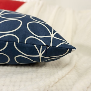 May include: Navy blue decorative pillow with a white floral pattern. The pillow has a zipper closure and is rectangular in shape. The pillow is resting on a white, textured surface.