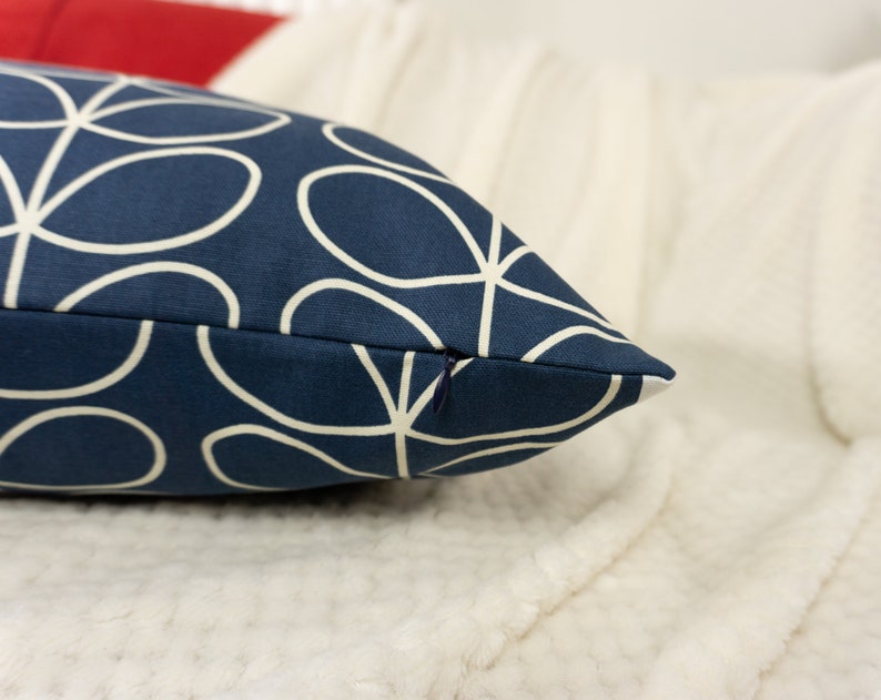 May include: Navy blue decorative pillow with a white floral pattern. The pillow has a zipper closure and is rectangular in shape. The pillow is resting on a white, textured surface.