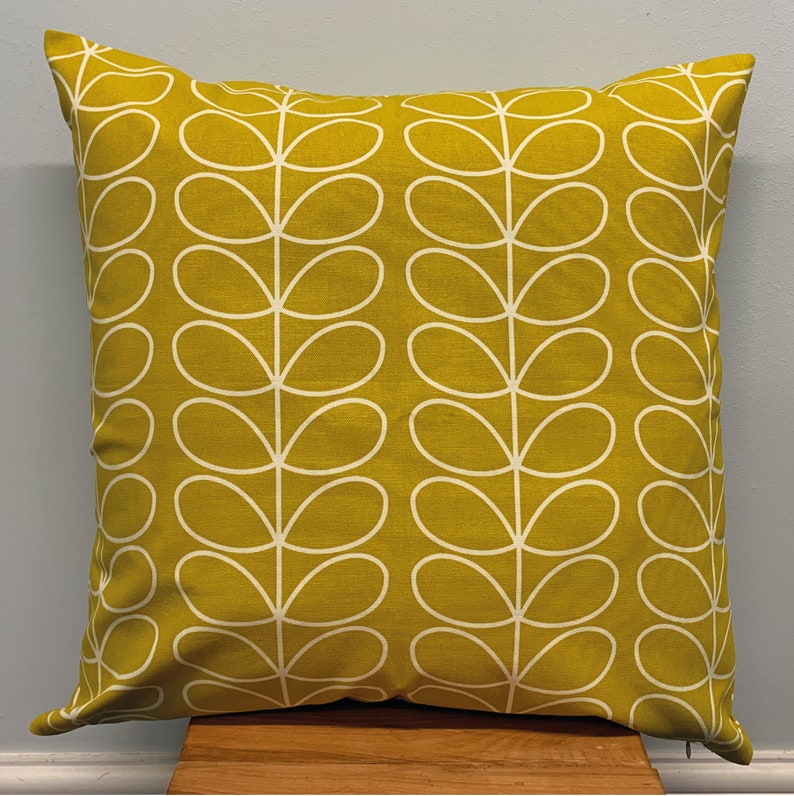 May include: Square decorative pillow with a mustard yellow background and a white leaf pattern. The pillow is made of fabric and has a zipper closure. The pillow is approximately 18 inches square.