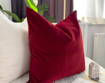 May include: A deep red velvet pillow on a white bed with a book and a small white decorative object.