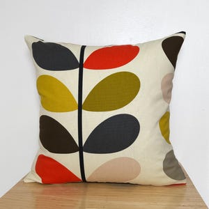 May include: Square decorative pillow with a cream background and a repeating leaf pattern in black, red, yellow, olive green, brown, and pink. The leaves are arranged along a central black stem.