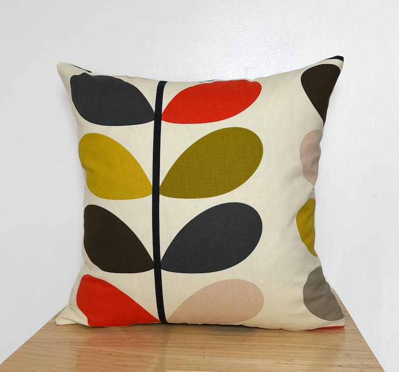May include: Square decorative pillow with a cream background and a repeating leaf pattern in black, red, yellow, olive green, brown, and pink. The leaves are arranged along a central black stem.