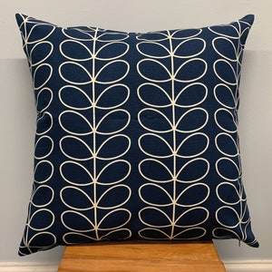 May include: Square navy blue throw pillow with a repeating white leaf pattern. The pillow is made of a soft fabric and is placed on a wooden surface. The design is modern and suitable for home decor.
