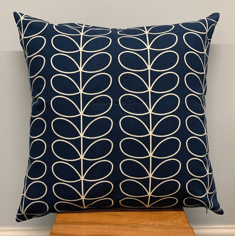 May include: Square navy blue throw pillow with a repeating white leaf pattern. The pillow is made of a soft fabric and is placed on a wooden surface. The design is modern and suitable for home decor.